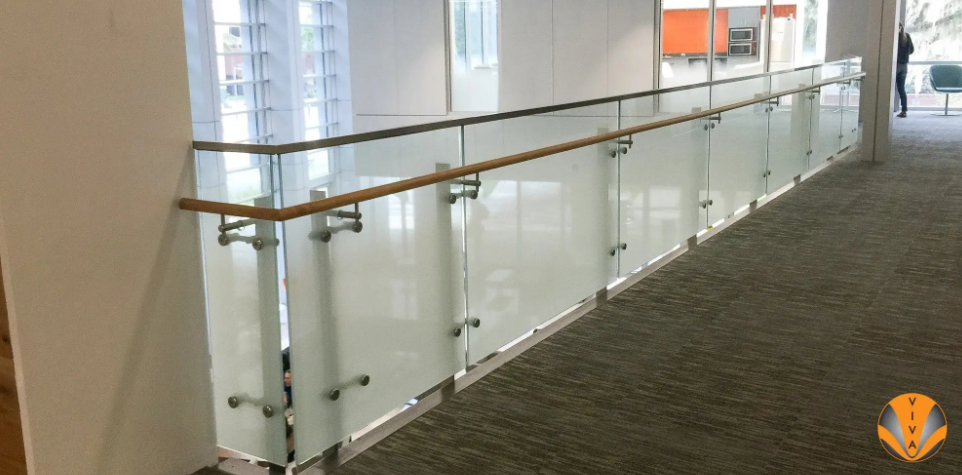 Interior glass railing with metal mounts and wood handrail along upper floor walkway.