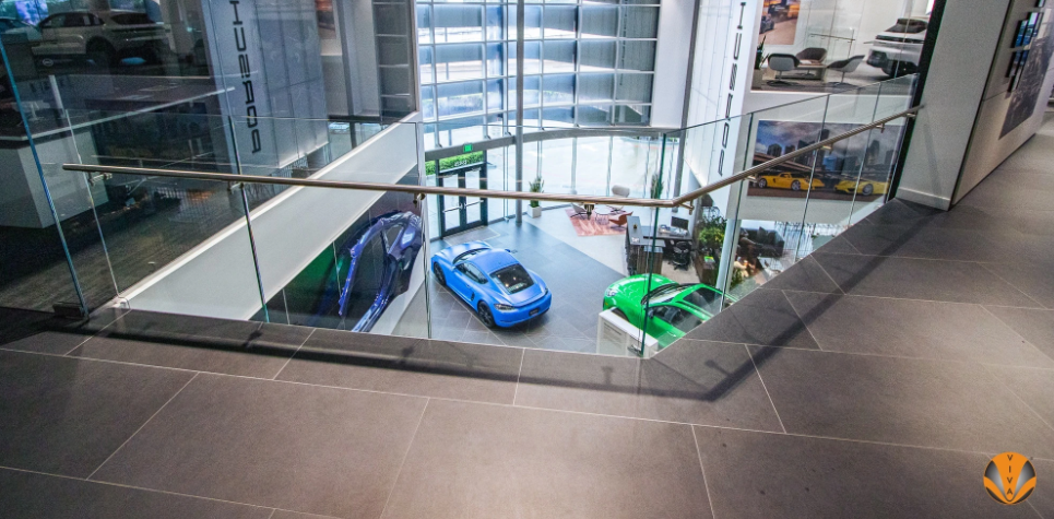 Glass railing overlooking modern showroom with cars below.