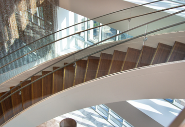Curved staircase with glass railings and wooden steps in a bright interior.