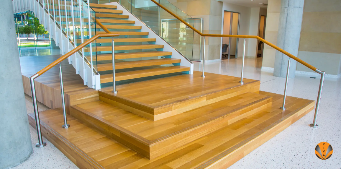Modern staircase with wood steps, glass railings, and metal handrails in commercial interior.
