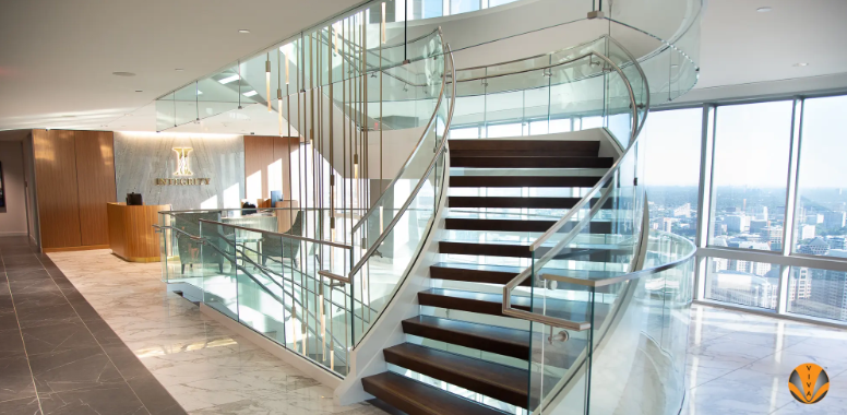 Curved glass staircase with metal railings in a modern office interior.