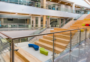 Modern interior with tiered wooden seating and glass railings in a multi-level building.