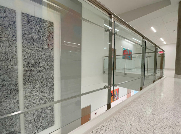 Interior hallway with post-supported glass railings overlooking lower level artwork.