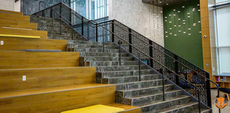 Tiered wooden seating and marble stairs with black metal railings in a modern interior space.