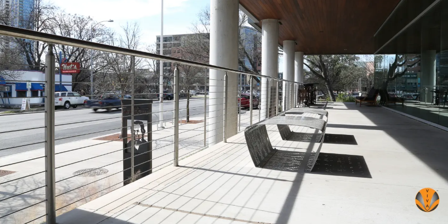 Stainless steel cable railing along a city sidewalk with modern benches.