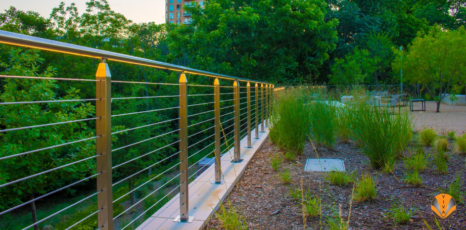 Outdoor stainless steel cable railing with integrated lighting in a landscaped area.