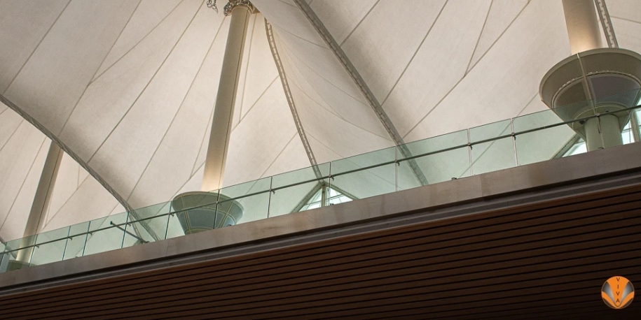 Sleek glass balcony railing with no visible frame under a large architectural canopy.