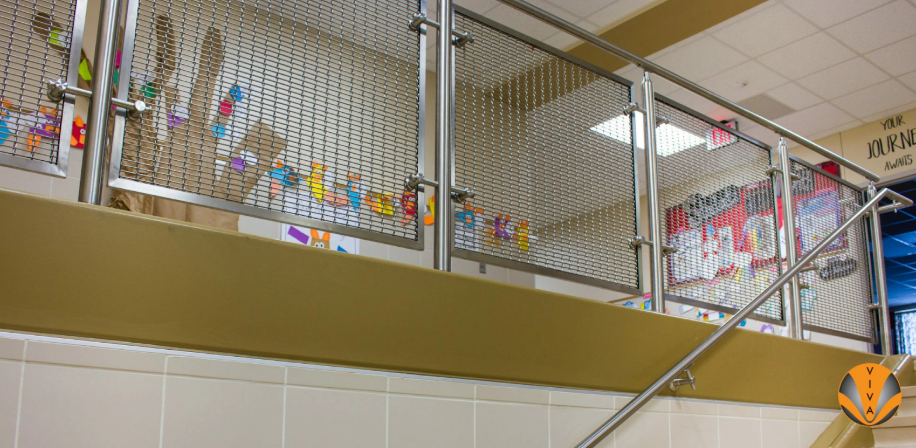 Staircase railing with stainless steel mesh infill panels in a modern school or office interior.