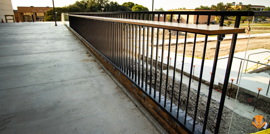 Outdoor metal railing with a sleek black powder-coated finish along a concrete walkway.