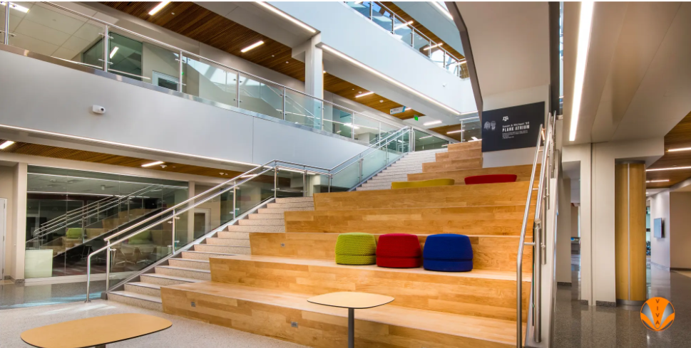 Modern atrium with tiered wooden seating, stairs, and glass railings.