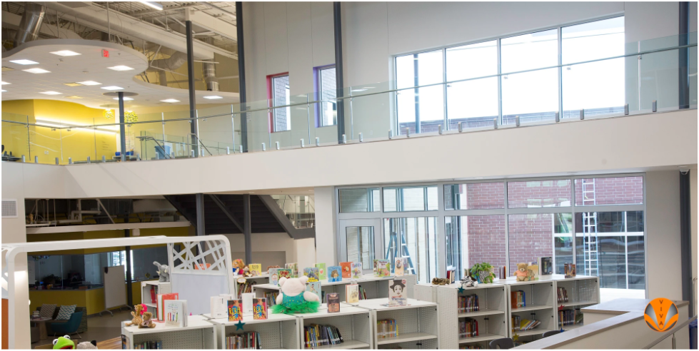 Modern school library with glass railings overlooking bookshelves and open learning spaces.