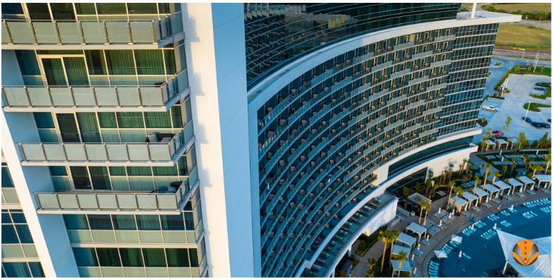 Aerial view of a modern hotel with glass balcony railings overlooking a large outdoor pool.