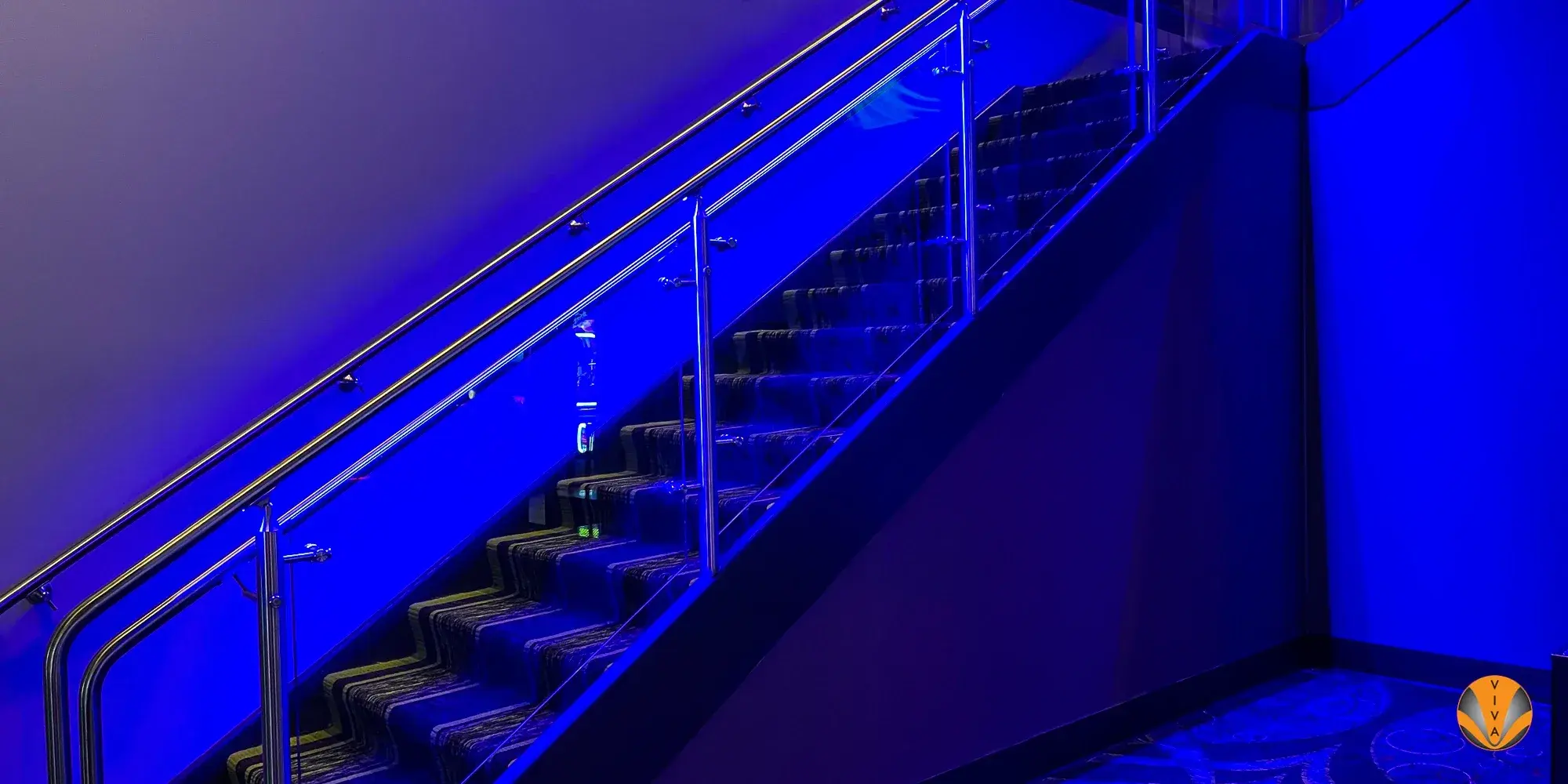 Commercial staircase with sleek metal railings illuminated by dramatic blue lighting.